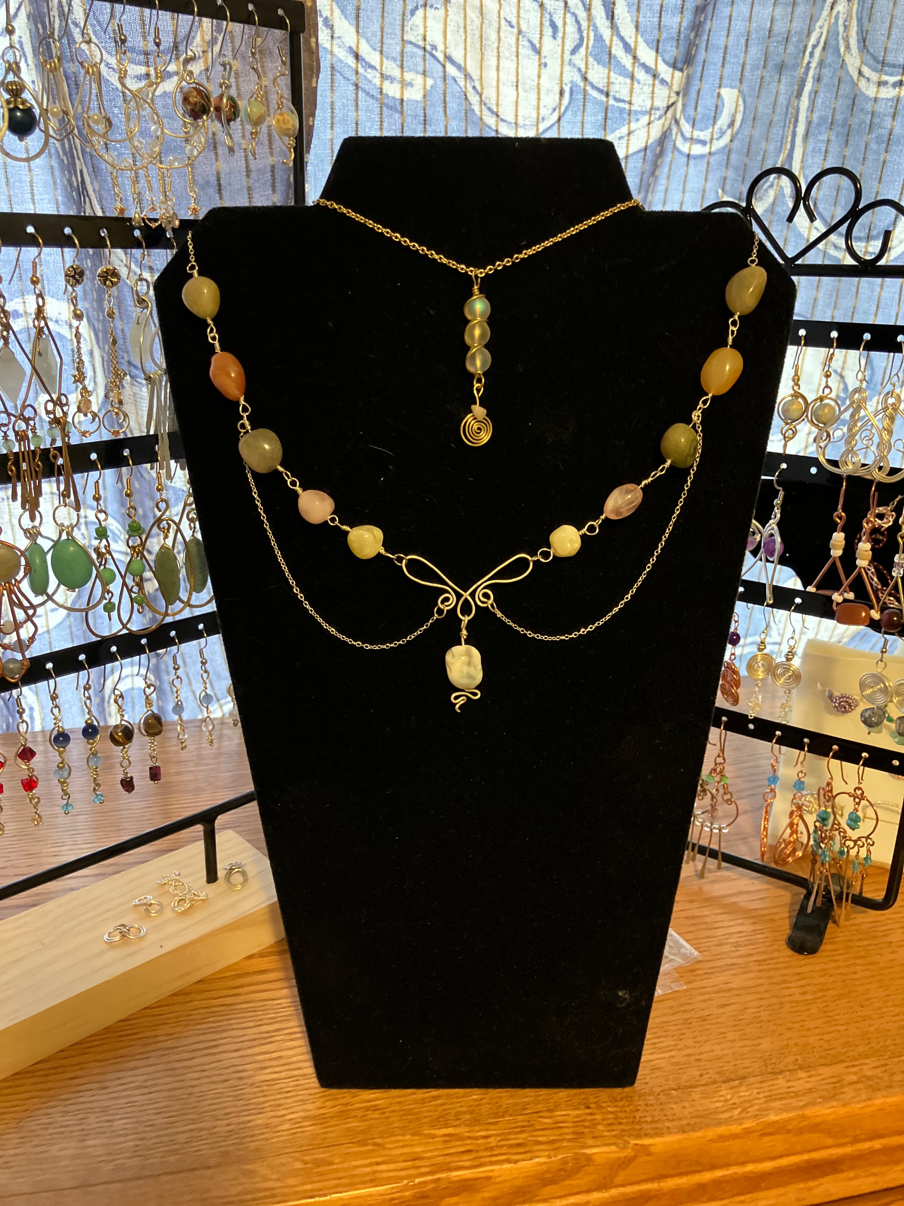 Black jewelry bust displaying two gold necklaces with colorful stone beads among various earring racks.