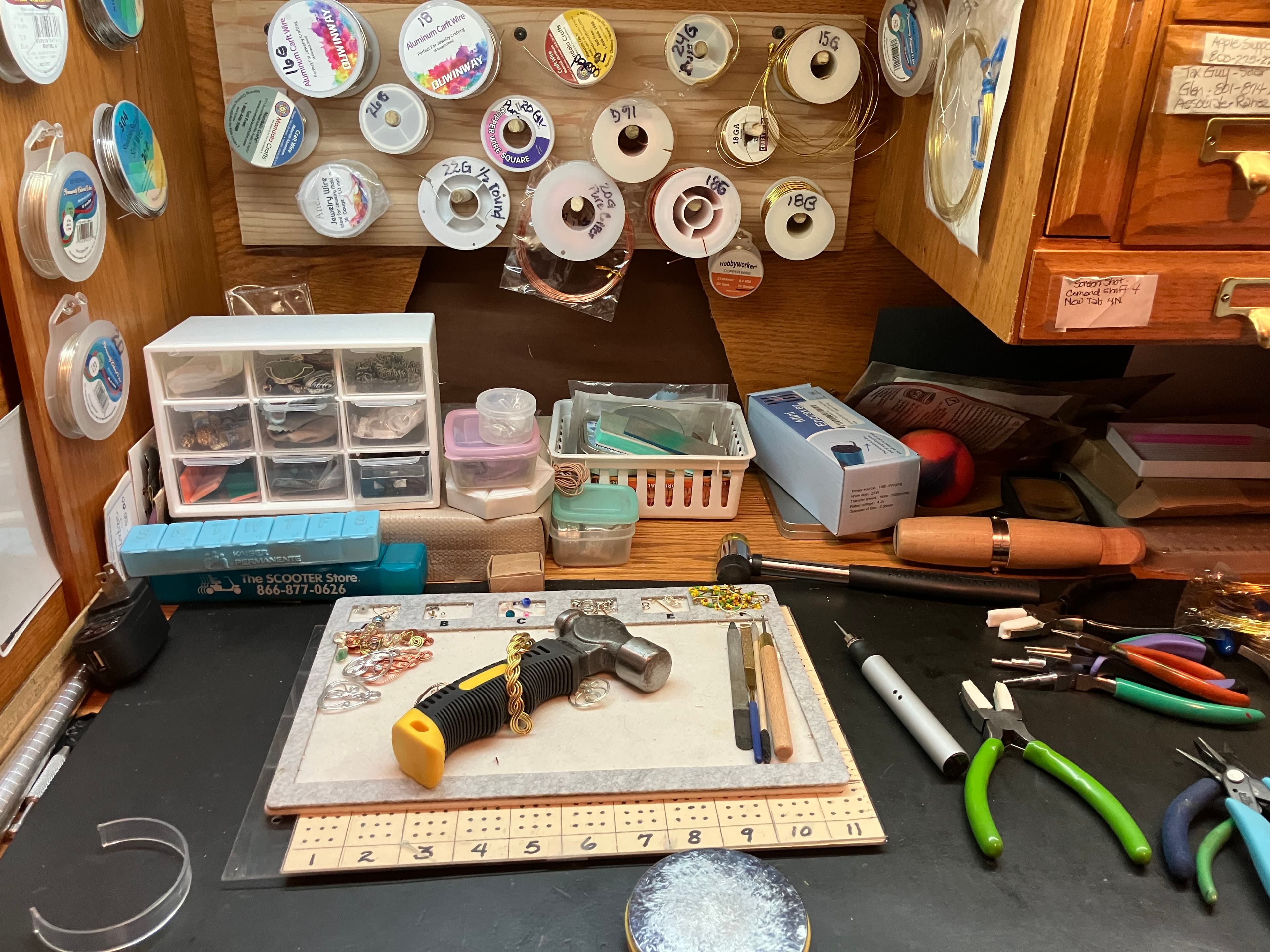 Organized jewelry-making workspace with wire spools, pliers, a hammer, and various crafting tools.